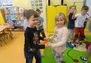 Dwoje dzieci stoi naprzeciw siebie trzymając wspólnie w dłoniach papierowe serduszko.